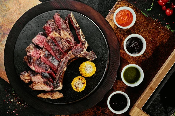 Kvašený steak. T-Bone Steak s grilovanou zeleninou na černém kulatém talíři na pozadí na měděném prostěradle. pohled shora. mezera pro text — Stock fotografie
