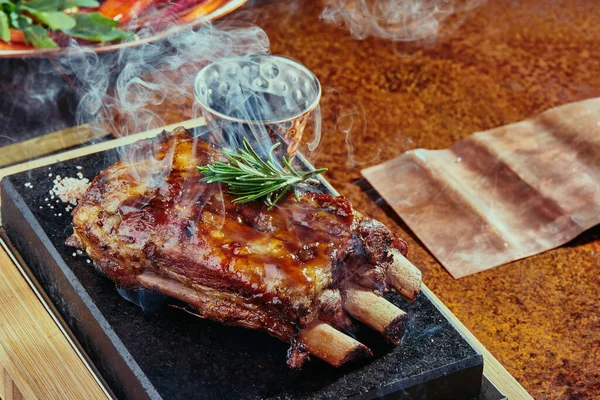 Barbekü soslu domuz pirzolası, siyah bir tabakta sigara, yeşil, baharat ve sebzelerden oluşan bir arka planda bakır bir çarşaf. Kapat..