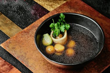 Kemikli şeffaf et suyu, maydanozla süslenmiş ve bakır arka planda siyah bir kasede Brüksel lahanası. Menü için. Bir dizi fotoğraf. yakın plan.