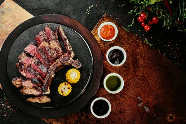 Kvašený steak. T-Bone Steak s grilovanou zeleninou na černém kulatém talíři na pozadí na měděném prostěradle. pohled shora. mezera pro text — Stock fotografie