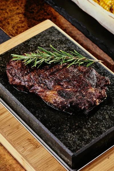 Fermentiertes Steak. Steak mit Rosmarin auf einem schwarzen Teller serviert mit gegrilltem Mais auf einem Hintergrund aus Gemüse, Gewürzen und frischem Gemüse, auf einem Kupferblech. Nahaufnahme. Fotoserie — Stockfoto