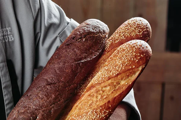 Γαλλικές μπαγκέτες. Ο φούρναρης κρατάει γαλλικές μπαγκέτες. Σκούρο και ελαφρύ ψωμί. Κλείσε. σειρά φωτογραφιών — Φωτογραφία Αρχείου