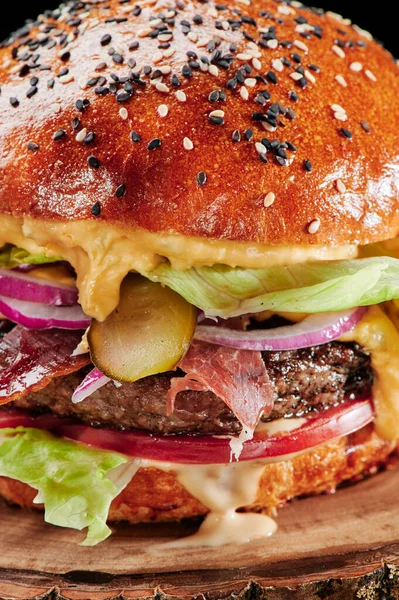 Marha burger sajttal, paradicsommal, vöröshagymával, uborkával és salátával fából készült háttérrel. Közelről. Egészségtelen élelmiszer — Stock Fotó