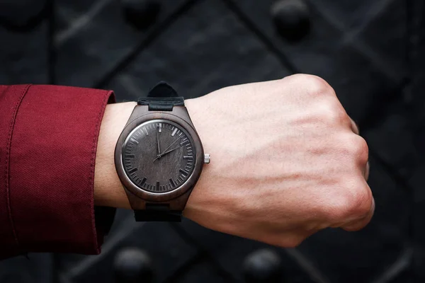 Hnědé dřevěné náramkové hodinky s koženým řemínkem na mužském zápěstí na černém pozadí. Detailní záběr. Mezera pro text. — Stock fotografie