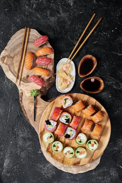 Sushi σετ με ρολό Φιλαδέλφεια, ρολό με αβοκάντο και ρολό με τόνο σε στρογγυλή ξύλινη σανίδα σε σκούρο φόντο. Άνω όψη — Φωτογραφία Αρχείου
