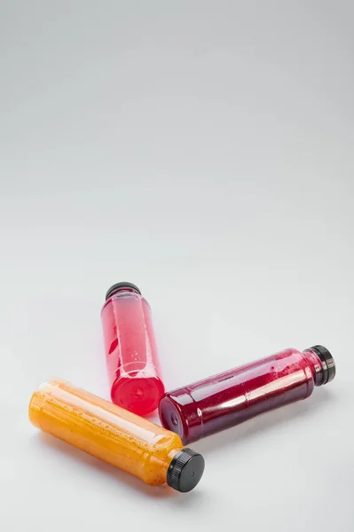 Plastikowe butelki nieprzetworzonych soków owocowych i warzywnych tłoczonych na zimno, jasnoszary stół. Oczyszczanie ciała, szybki pomysł. Minimalistyczna fotografia żywności. Przestrzeń kopiowania — Zdjęcie stockowe