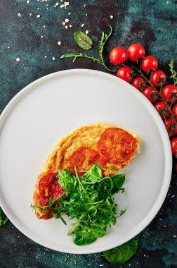 Sağlıklı kahvaltı. Fırında domatesli omlet ve oksitlenmiş mavi arka planda beyaz tabakta ıspanak salatası. Üst görünüm