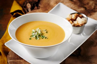 Beyaz tabakta balkabağı kremalı çorba, ahşap kesim, paslı arka planda. Menü ve site için fotoğraf. Metin için boşluk