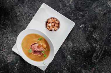 Beyaz tabakta pastırmalı balkabağı kremalı çorba ve dokulu koyu arka plan. Sağlıklı organik gıda konsepti. Üst görünüm