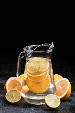 Sürahide sağlıklı limonata. Limonlu narenciye kokteyli, siyah arka planda turuncu.