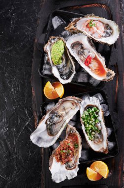 Buzlu ve limonlu tabakta çeşitli taze istiridyeler. Arka planda siyah dokular, üst manzara.