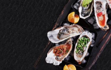 Buzlu ve limonlu tabakta çeşitli taze istiridyeler. Arka planda siyah dokular, üst manzara.