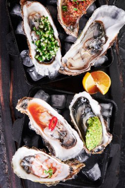 Buzlu ve limonlu tabakta çeşitli taze istiridyeler. Arka planda siyah dokular, üst manzara.