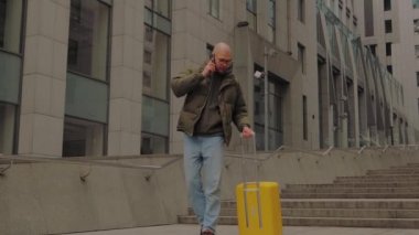 Avrupalı bir adam ofis merkezinden sarı bavulla gelir, telefonla konuşur. İş gezisi