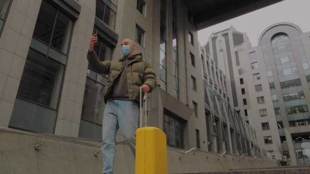 Hombre europeo saliendo del centro de oficina con maleta amarilla y habla cara a cara en máscara protectora — Vídeo de stock