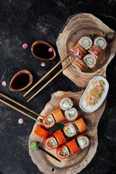 Sushi rolls California and Philadelphia on wooden cut on black background. Concept delivery service. Top view. Japan food in eco container. Zero waste packaging — Photo