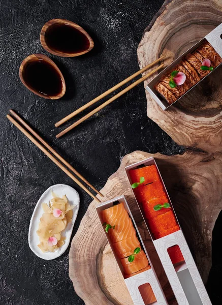 Set of California and Philadelphia sushi rolls in disposable paper boxes on wooden cut. Delivery service concept. Japanese food in eco-container. Top view. Waste-free packaging — Photo