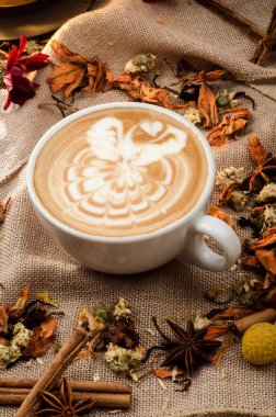 Baharatla süslenmiş çuval bezinin arka planında köpüklü güzel desenli kapuçino kahvesi. Kapatın. Metin için boşluk