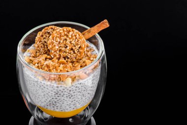 Siyah arka planda izole edilmiş şeffaf bir bardakta mango ve kozinakili Chia pudingi. Metin için boşluk