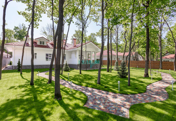 Backyard of modern white country house with brown roof and beautiful garden. Well-groomed beautiful lawn. Space for text