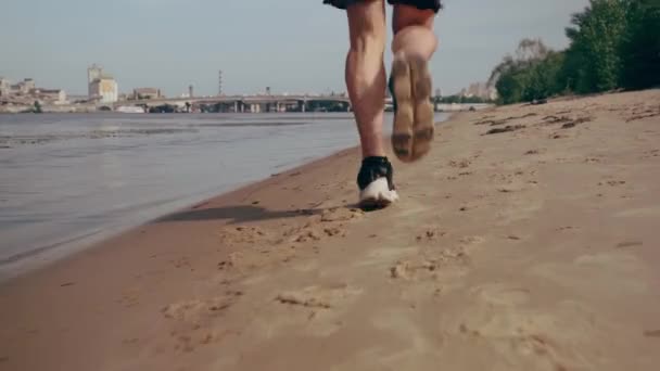 Muscular young man running on the beach on sunny day. Cardio exercise. Tracking camera — Stock Video