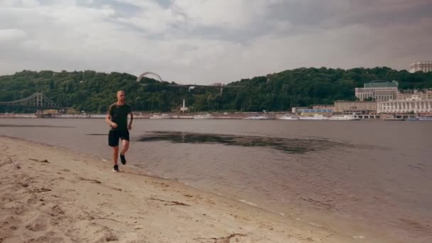 晴れた日に市内のビーチを走る筋肉質の若い男。心臓運動だ。朝のランニング — ストック動画