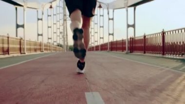 Siyah spor üniformalı genç adam şafak vakti yaya köprüsünde koşar. Yavaş çekim