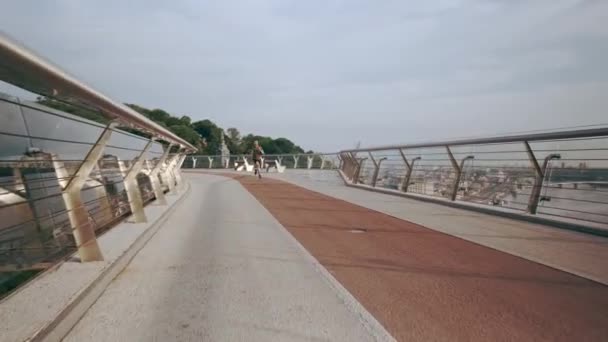 Un joven con uniforme deportivo corre por el puente peatonal al amanecer. Movimiento lento — Vídeo de stock