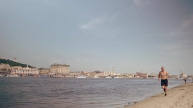 Güneşli bir günde şehrin sahilinde koşan kaslı genç adam. Kardiyo egzersizi. Sabah koşusu
