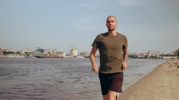 Un joven musculoso corriendo por la playa en un día soleado. Ejercicio cardiovascular. Mañana corriendo — Vídeo de stock