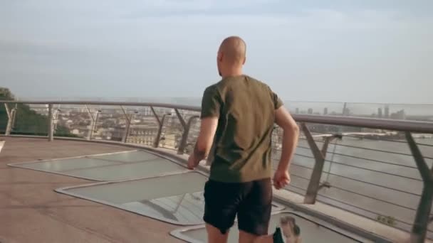 Un joven con uniforme deportivo corre por el puente peatonal al amanecer. Movimiento lento — Vídeo de stock