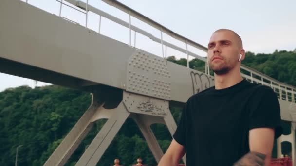 Hombre corredor en uniforme deportivo negro estirando las manos antes de los deportes en el puente peatonal al amanecer — Vídeos de Stock