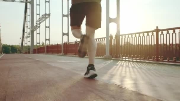 Un joven con uniforme deportivo negro corre por el puente peatonal al amanecer. Movimiento lento — Vídeo de stock