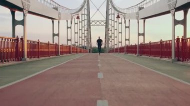 Siyah spor üniformalı genç adam şafak vakti yaya köprüsünde koşar. Yavaş çekim