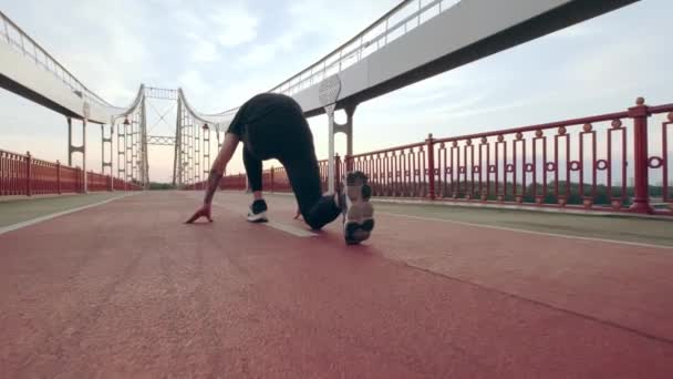 Un joven con uniforme deportivo negro corre por el puente peatonal al amanecer. Comienzo bajo. Movimiento lento — Vídeo de stock