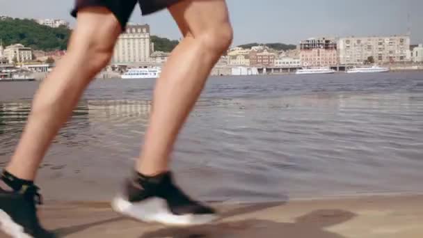 Muscular young man running on the beach in the city on a sunny day. Cardio exercise. Tracking camera — Stock Video