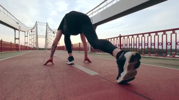 Un joven con uniforme deportivo negro corre por el puente peatonal al amanecer. Comienzo bajo. Movimiento lento — Vídeo de stock