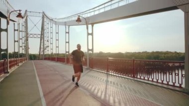 Atletik genç adam şafakta şehirdeki yaya köprüsünde koşar. Etkin yaşam tarzı kavramı
