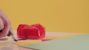 Pasta şefi kırmızı pastayı sarı arka planda kalp şeklinde keser. Pasta dolumu