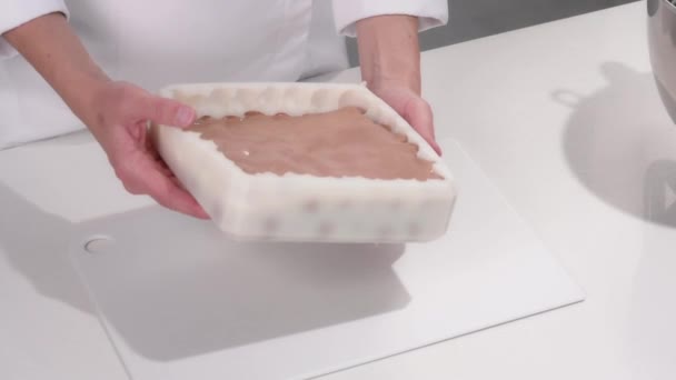 Chef pâtissier verse la crème brune dans un moule à gâteau en silicone. Cuisiner un dessert mousse. — Video