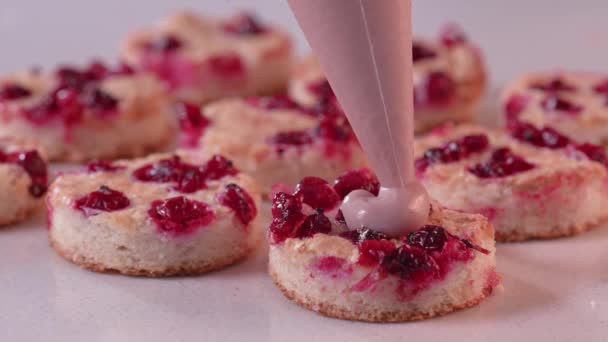 De banketbakker perst roze room uit een banketbakje op de minitaart. Minicake in elkaar zetten. — Stockvideo