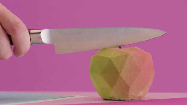 Кондитер режет фирменный десерт в виде яблока на цветном розовом фоне. Заправка тортов — стоковое видео