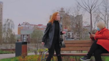 Koruyucu maskesi olmayan bir kadın parkta maske takan bir kadına oturuyor. Kadın gidiyor. Salgın