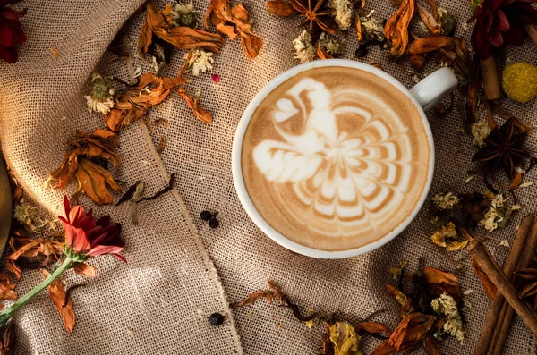 Cappuccino koffie met prachtig patroon op schuim in witte beker op de achtergrond van jute versierd met specerijen. Sluit maar af. Ruimte voor tekst. — Stockfoto