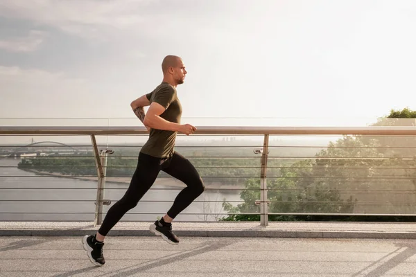 Young European man runs on the pedestrian bridge in the city at dawn. Healthy lifestyle concept