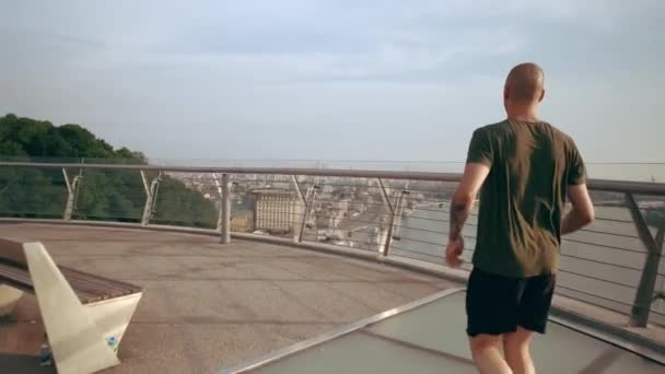 Young man in sports uniform runs on the pedestrian bridge at dawn. Slow motion — Stock Video