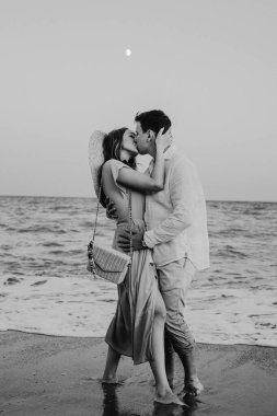 Mutlu genç çift sahilde yürüyor ve öpüşüyor. Siyah beyaz fotoğraf