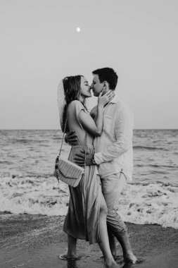 Mutlu genç çift sahilde yürüyor ve öpüşüyor. Siyah beyaz fotoğraf