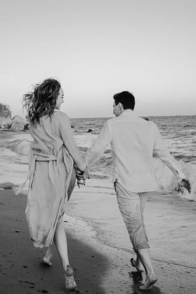 Ritratto di felice giovane coppia europea sta correndo lungo la costa. Stile di vita felice. Foto in bianco e nero — Foto Stock
