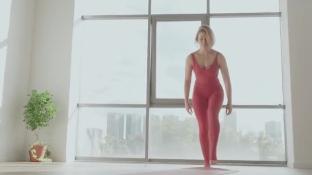 Mujer en uniforme deportivo rojo despliega esterilla deportiva y practica yoga en el estudio. Estilo de vida saludable — Vídeos de Stock